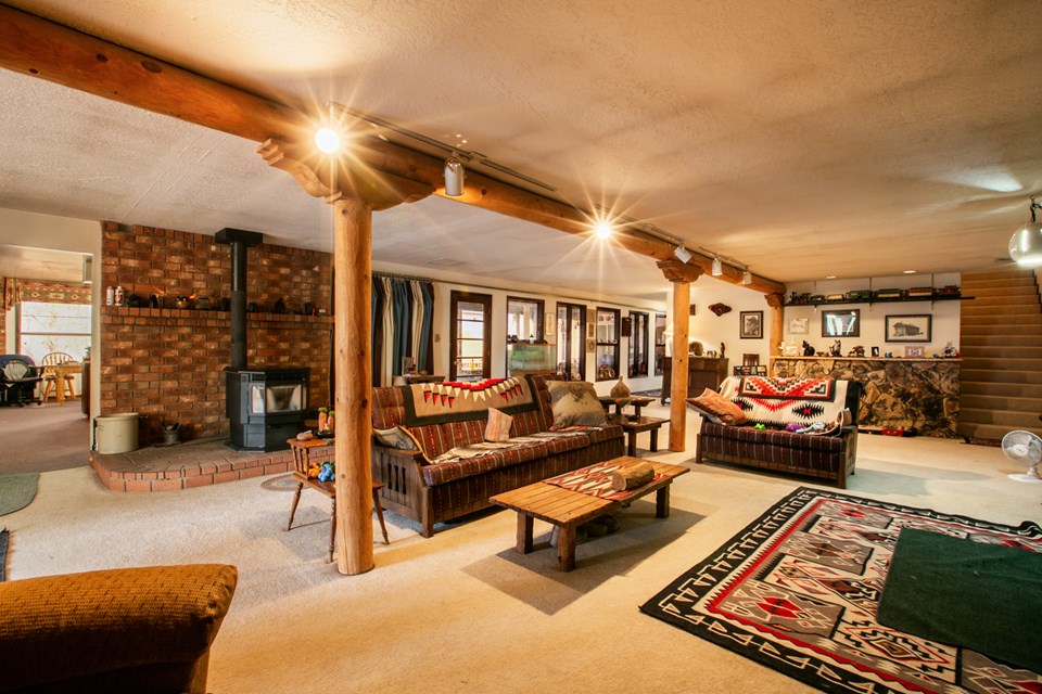 view of the great room from the living room. looking into the kitchen at left, pellet stove along short brick wall and a wet bar at the end.